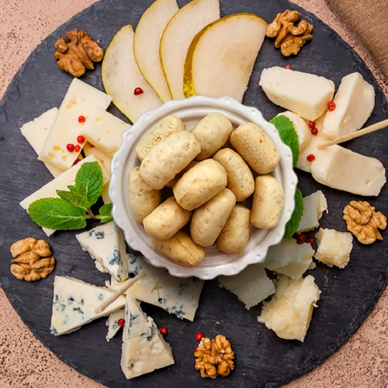 I Macoritti mini breadsticks served on a platter with assorted cheeses, pear slices, walnuts, and mint leaves