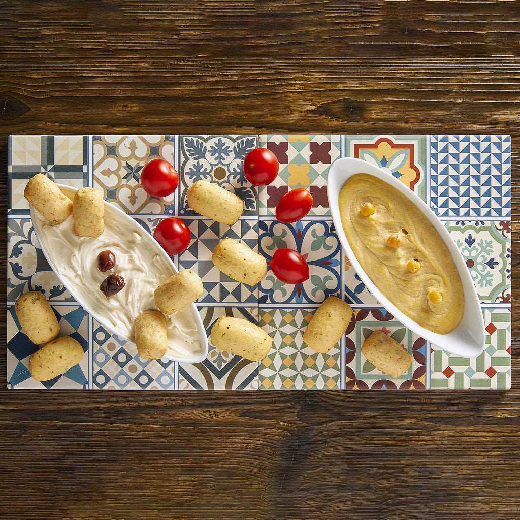 I Macoritti Snack mini breadsticks served with creamy dip and hummus alongside cherry tomatoes on patterned tile board